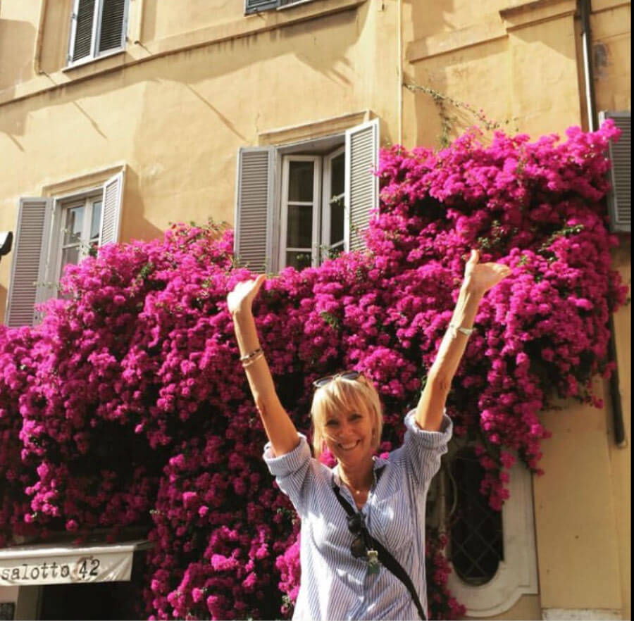 Debra Hutton raising her arms in from of a beautiful pink Bougainvillea in Italy